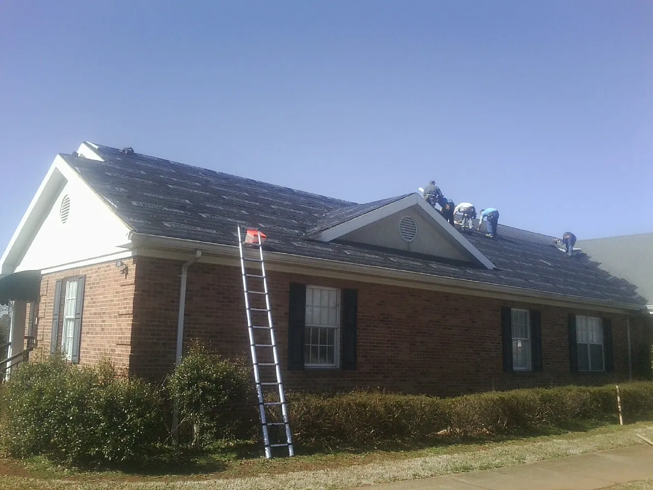Crew tearing shingles off a brick ranch roof with a ladder set — Metal Roof Repair work by our crew in Pinson